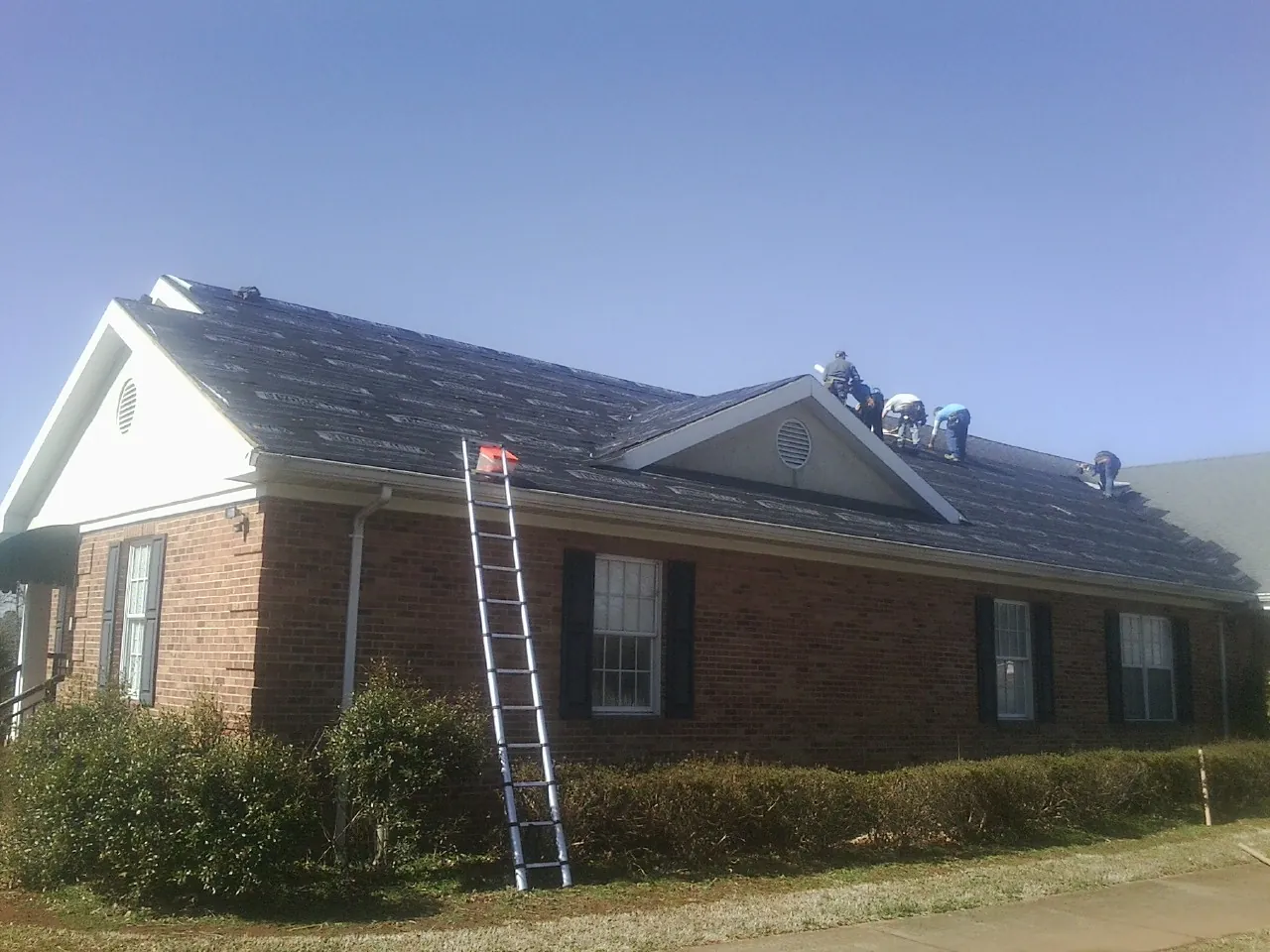 Crew tearing shingles off a brick ranch roof with a ladder set — Metal Roof Repair work by our crew in Allenwood